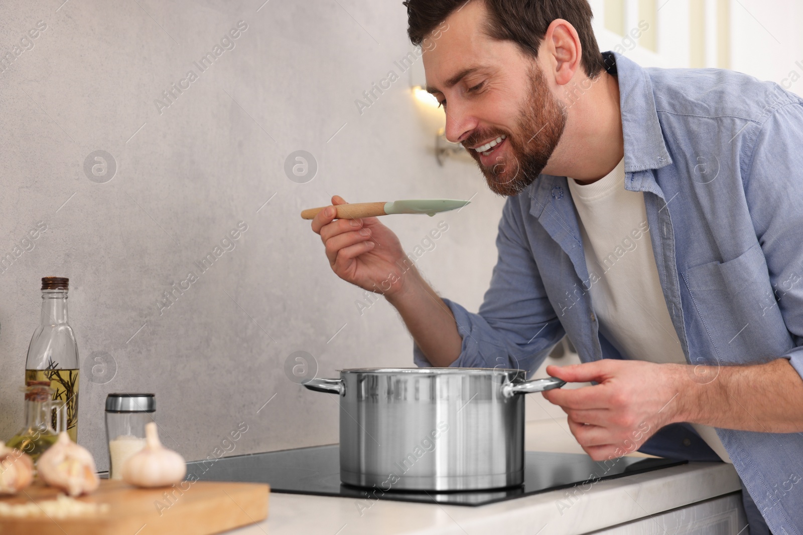 Photo of Man tasting delicious chicken soup in kitchen