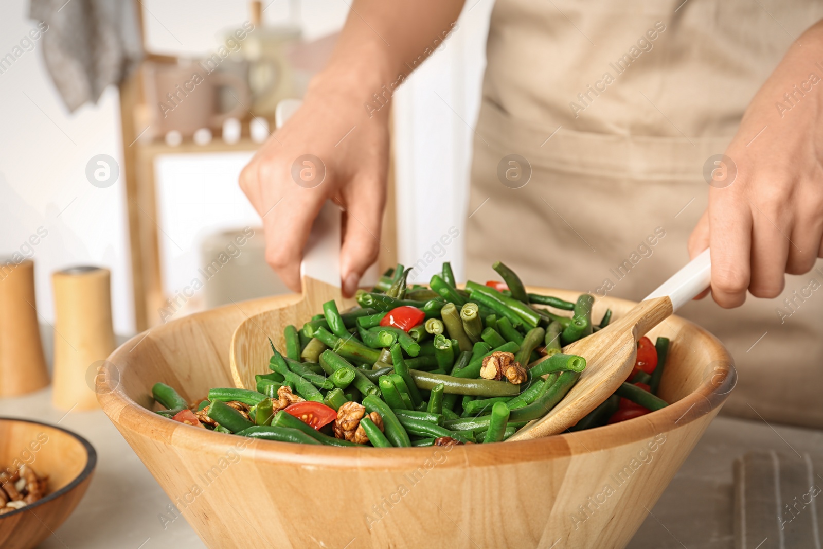 Photo of Woman preparing healthy salad with green beans, cherry tomatoes and walnuts at table