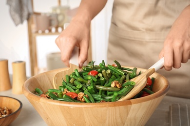 Photo of Woman preparing healthy salad with green beans, cherry tomatoes and walnuts at table