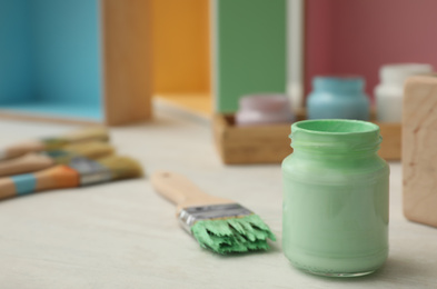 Photo of Jar of green paint and brush on white table, closeup. Space for text