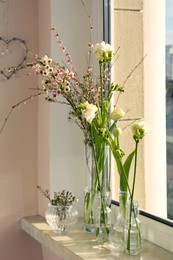 Many different spring flowers and branches with leaves on windowsill indoors
