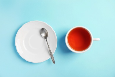 Cup of delicious tea with saucer and spoon on color background, top view