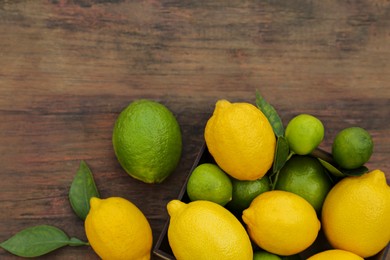 Photo of Many fresh lemons and limes with leaves on wooden table, flat lay. Space for text