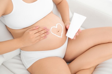 Heart painted with body cream on pregnant woman's belly at home, closeup