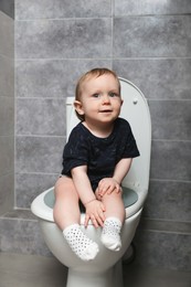 Photo of Little child sitting on toilet bowl indoors
