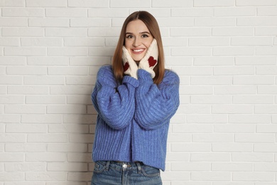 Beautiful young woman in mittens and blue sweater near white brick wall. Winter season