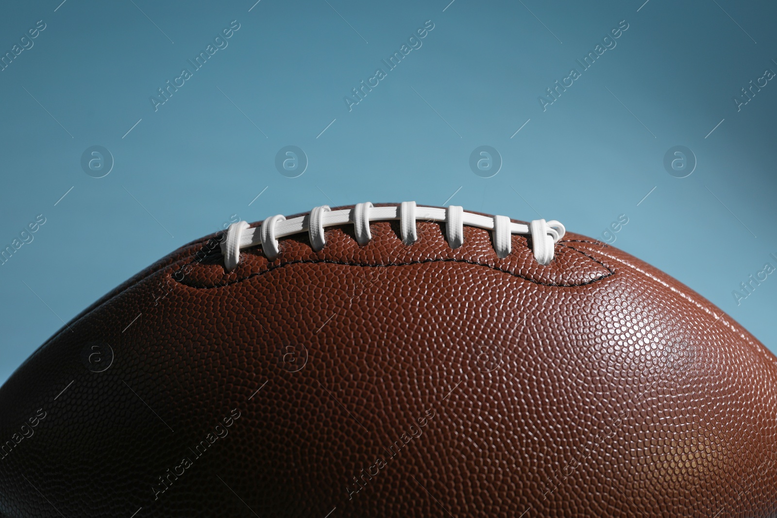 Photo of American football ball on light blue background, closeup