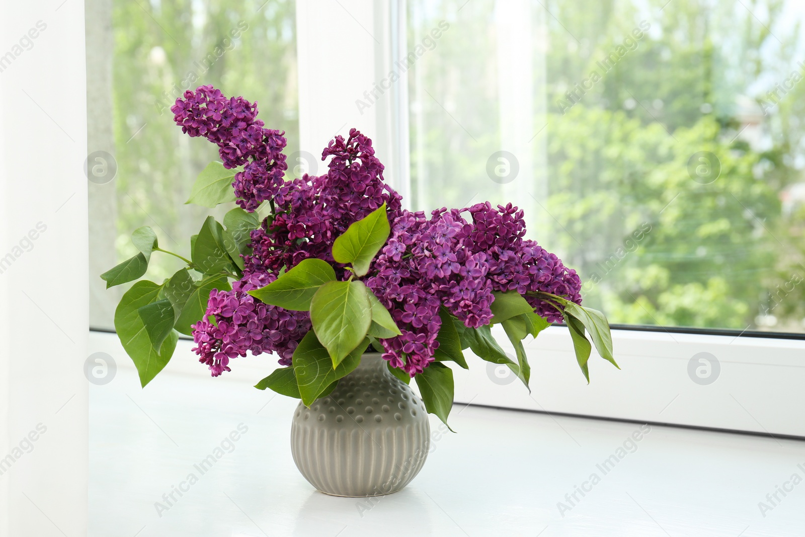 Photo of Beautiful lilac flowers in vase on windowsill