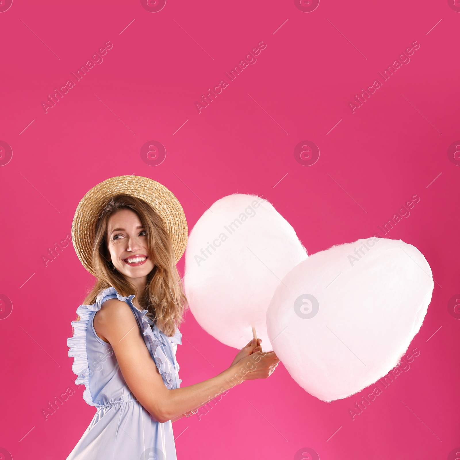 Photo of Happy young woman with cotton candies on pink background