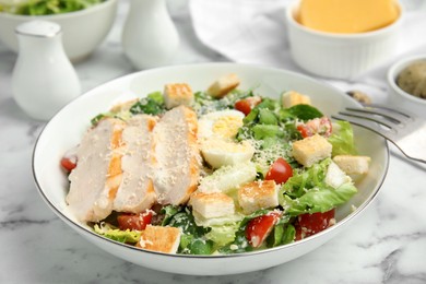 Photo of Delicious Caesar salad in bowl on white marble table, closeup