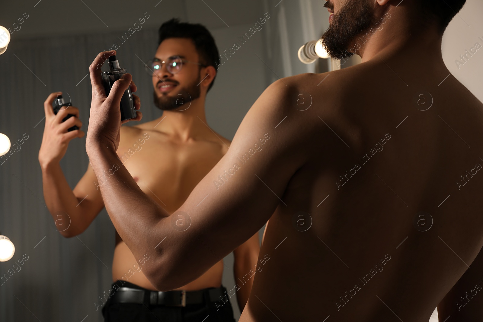 Photo of Man spraying luxury perfume near mirror indoors