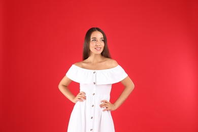 Young woman wearing stylish white dress on red background