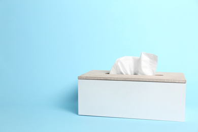 Photo of Holder with paper tissues on light blue background. Space for text