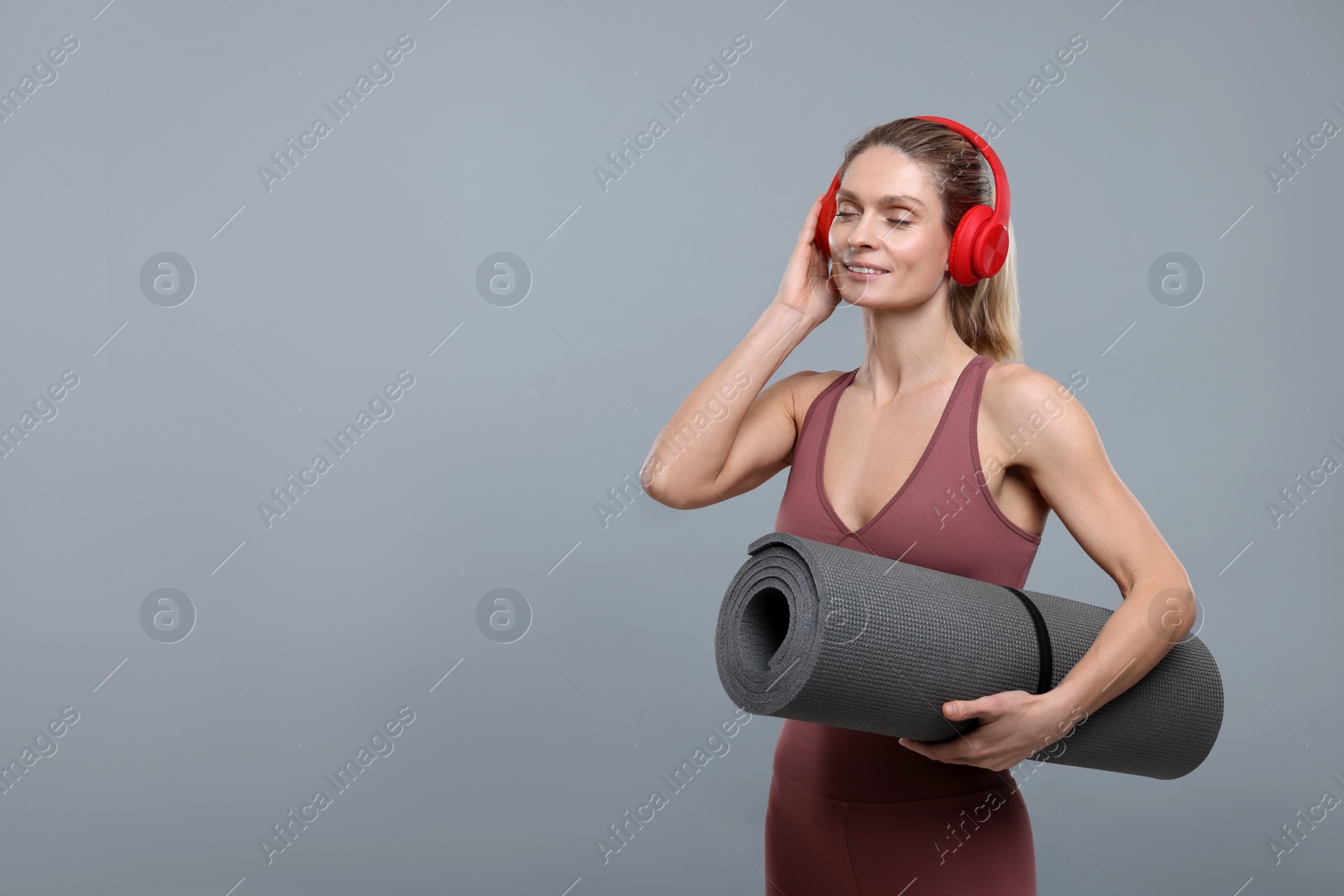 Photo of Sportswoman with headphones and fitness mat on grey background, space for text