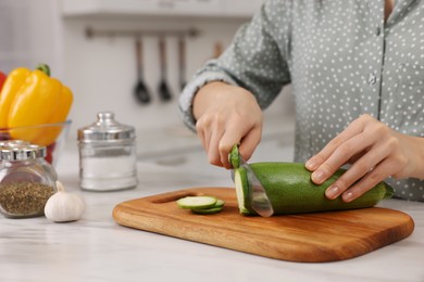 Photo of Cooking process. Woman cutting zucchini at white marble countertop in kitchen, closeup