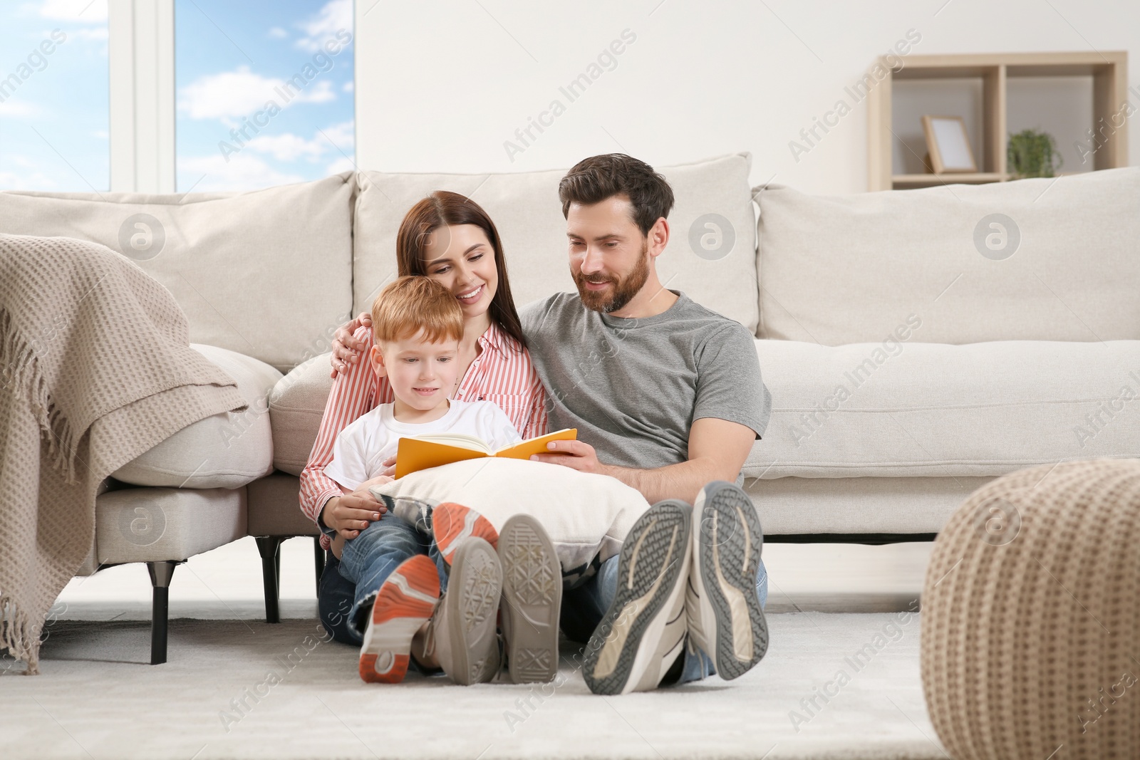 Photo of Happy parents with their child reading book on floor at home