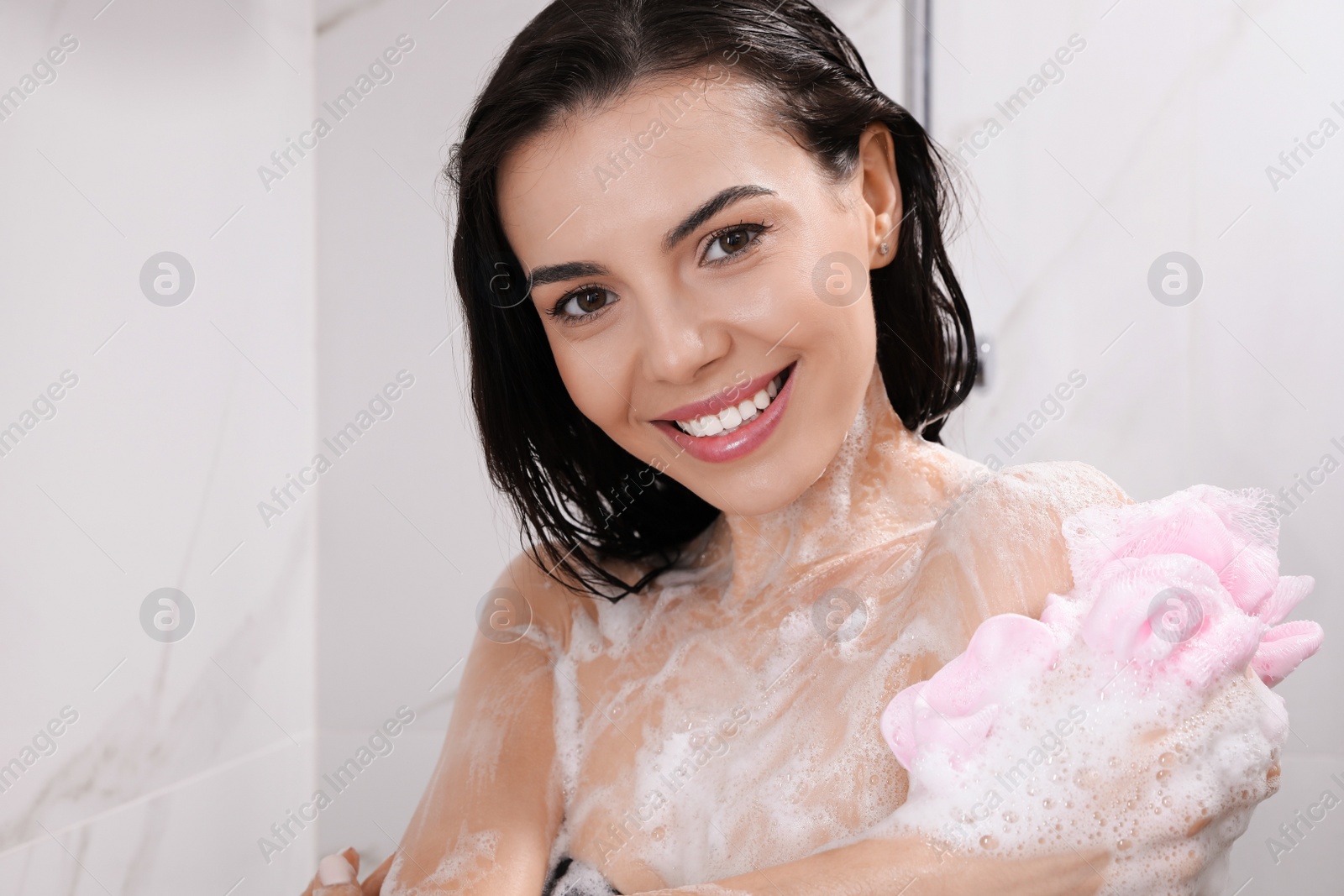 Photo of Young woman with mesh pouf taking shower at home