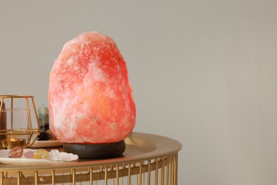Photo of Himalayan salt lamp, candle and crystals on golden table near light grey wall, space for text