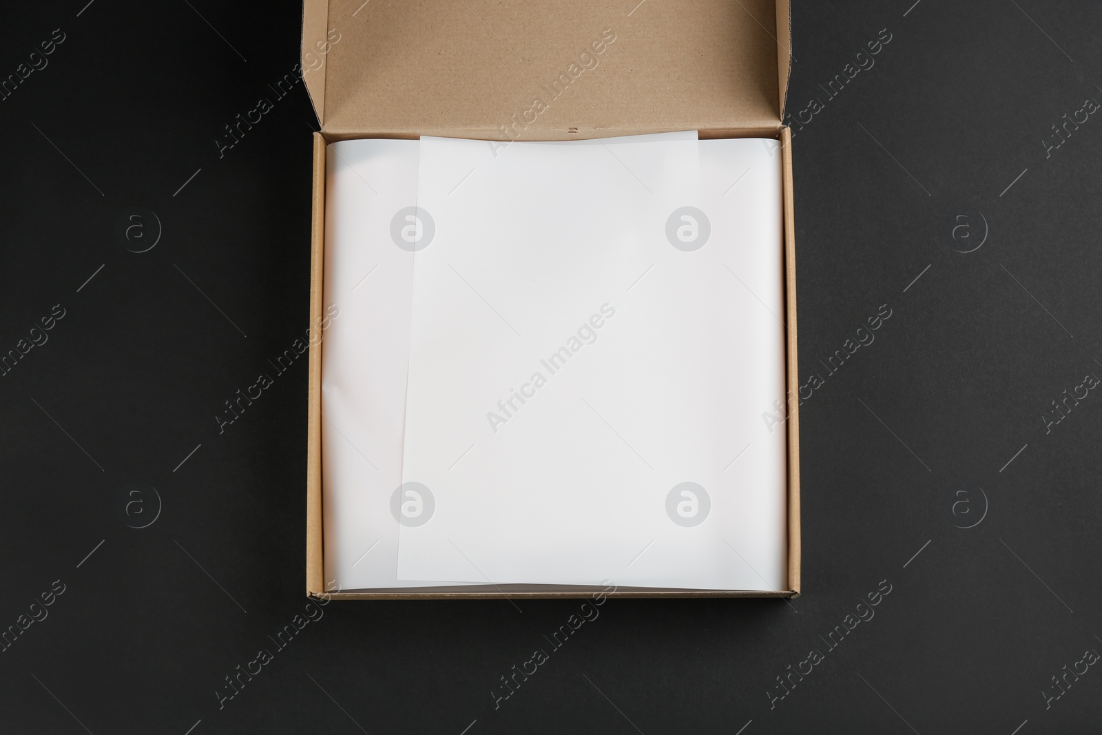 Photo of Cardboard box with parchment on black background, top view