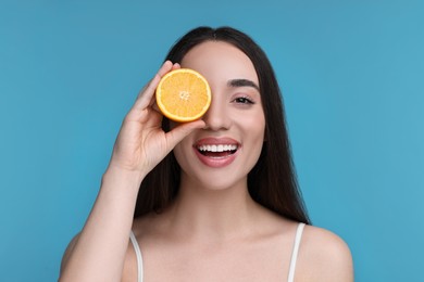 Photo of Beautiful young woman with piece of orange on light blue background