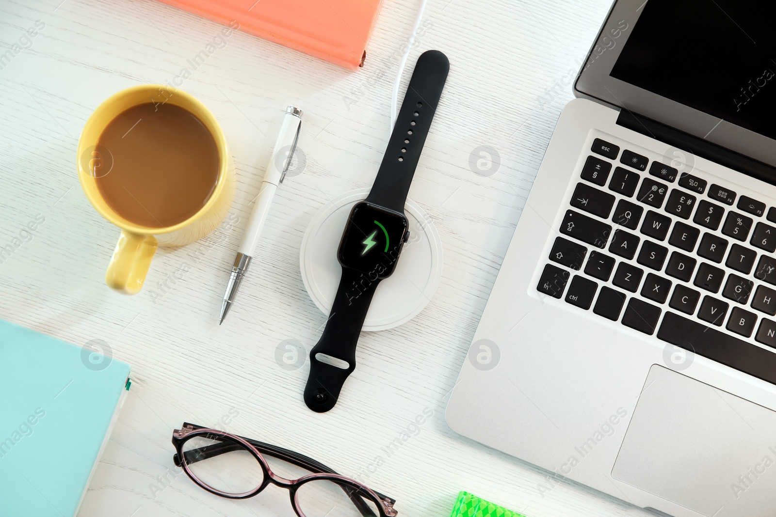 Photo of Flat lay composition with smartwatch and wireless charger on white wooden table. Modern workplace accessory