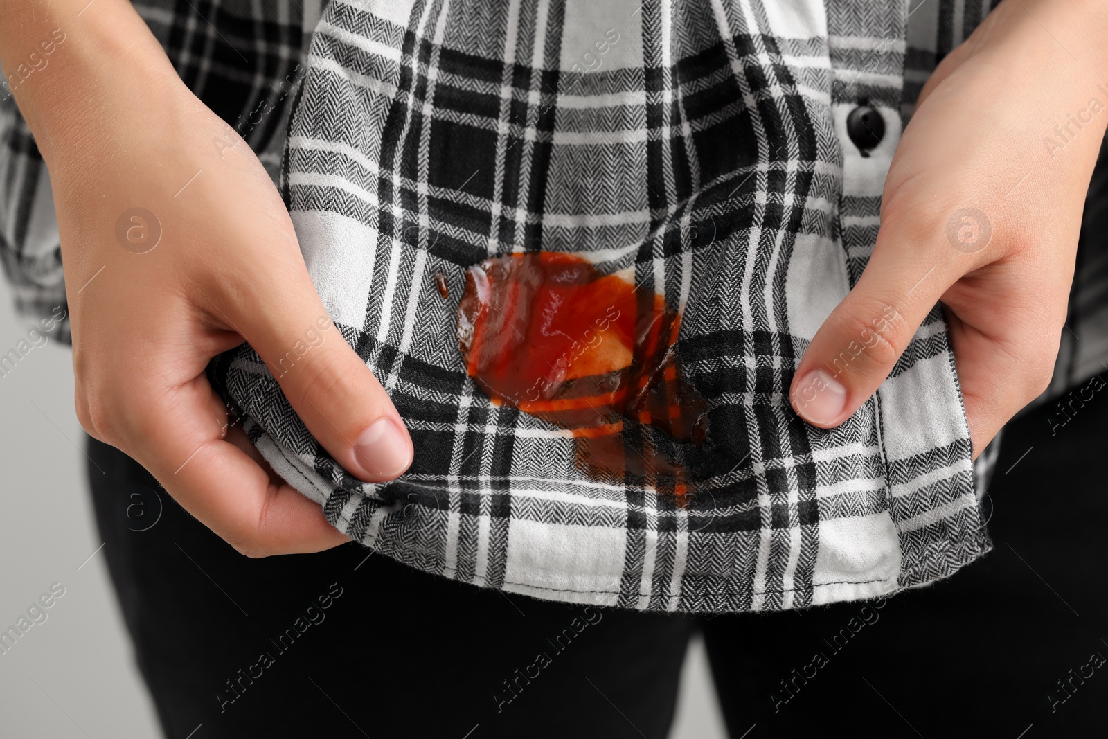 Photo of Woman showing sauce stain on her shirt against grey background, closeup