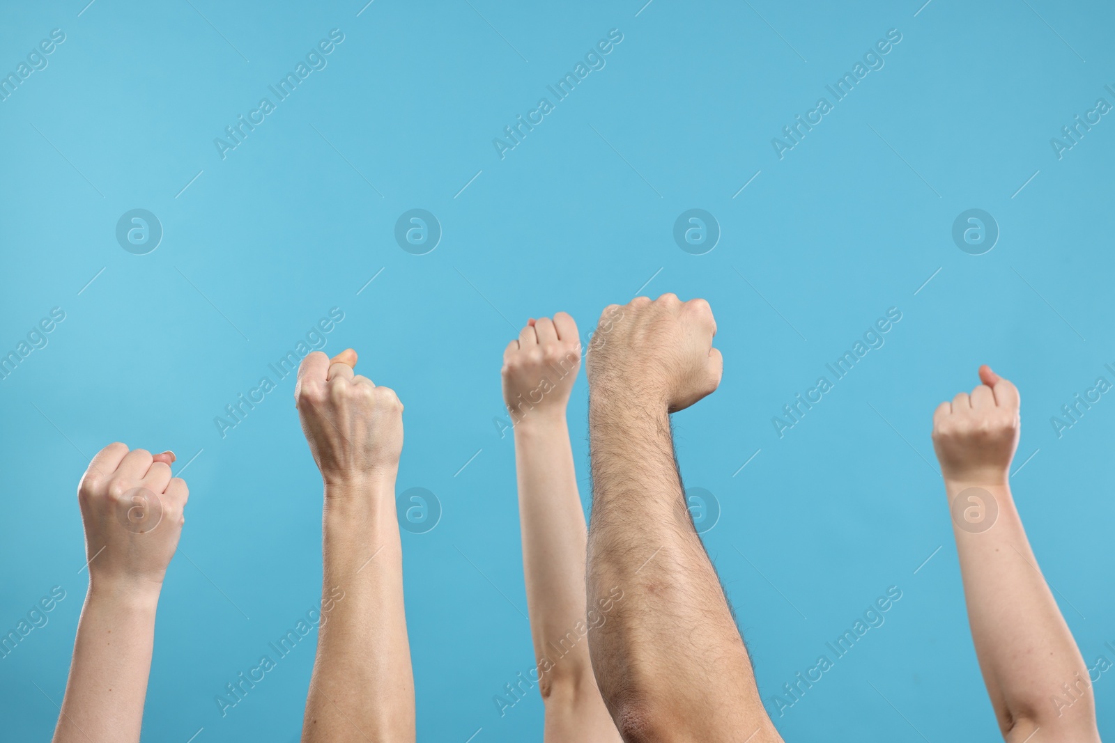 Photo of Strike. People showing clenched fists on light blue background, closeup
