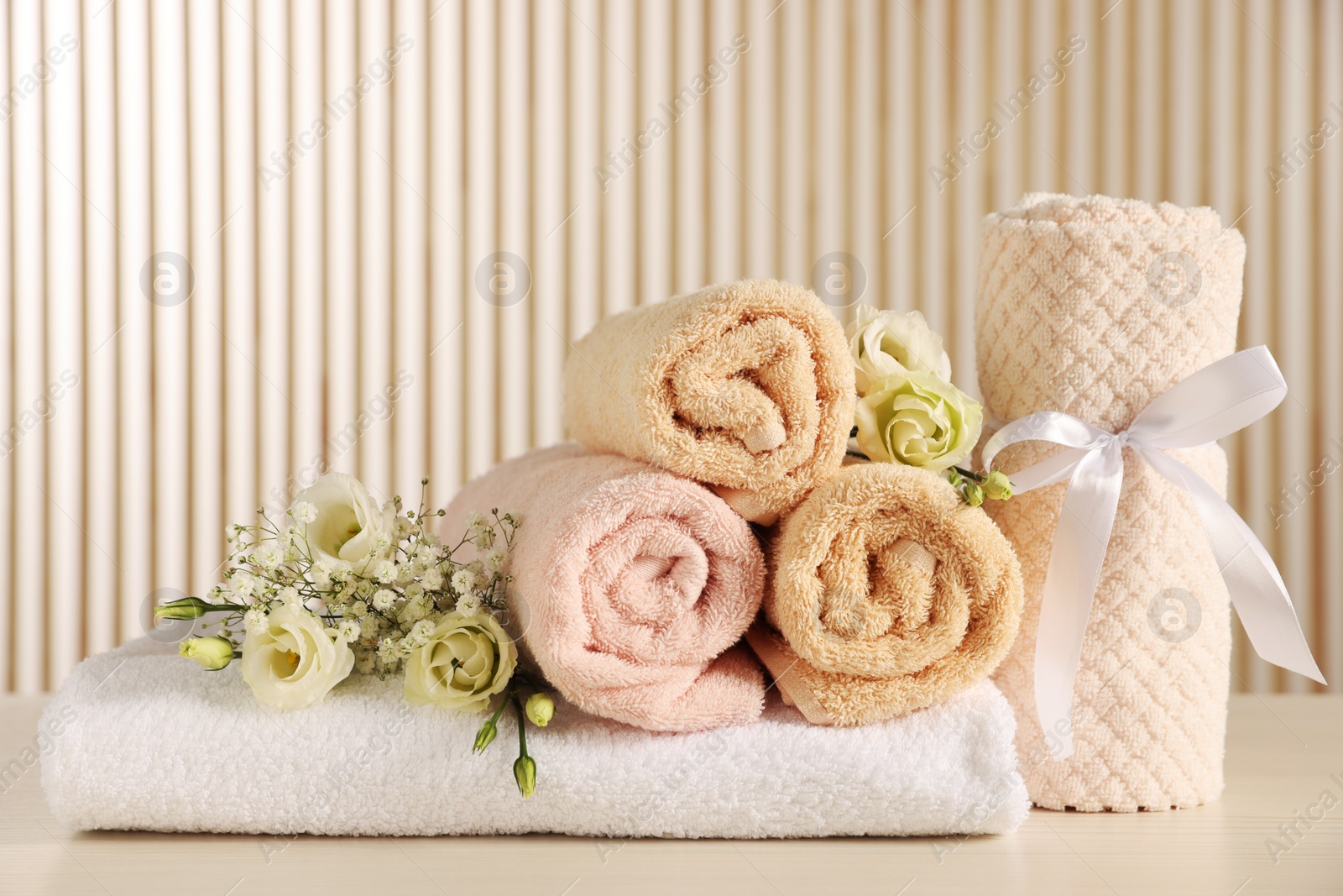 Photo of Soft towels, gypsophila and eustoma flowers on light wooden table