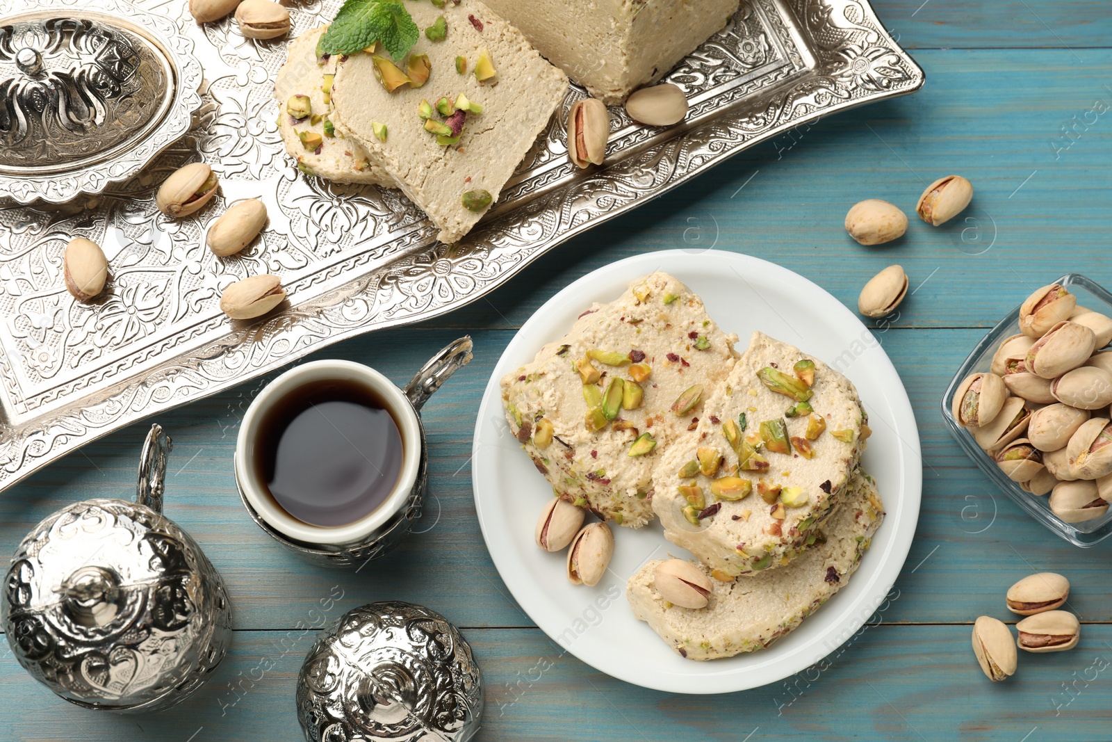 Photo of Tasty halva with pistachios served on light blue wooden table, flat lay