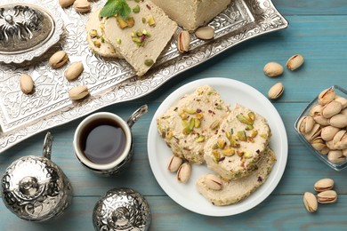 Photo of Tasty halva with pistachios served on light blue wooden table, flat lay