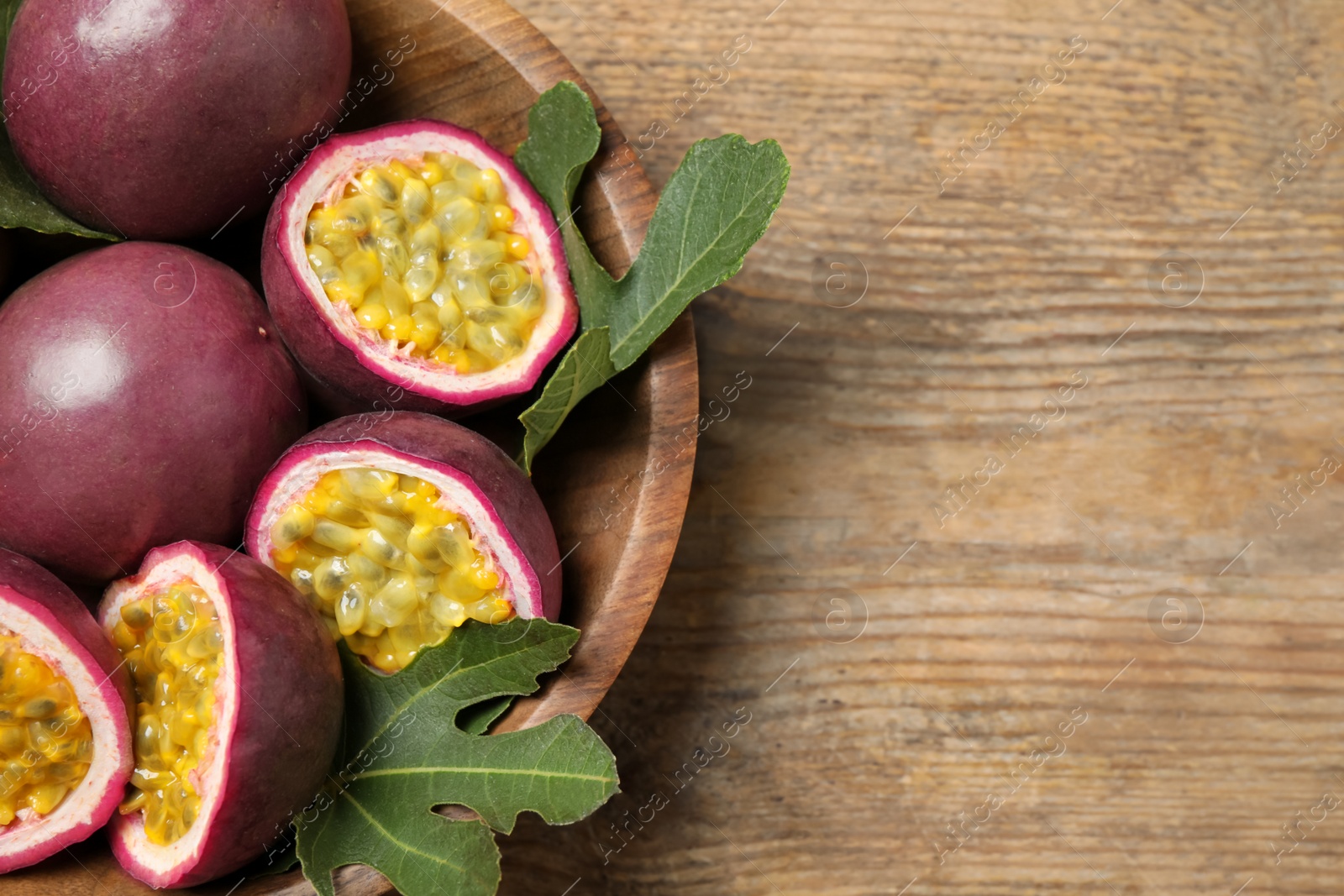 Photo of Cut and whole passion fruits (maracuyas) on wooden table, top view. Space for text