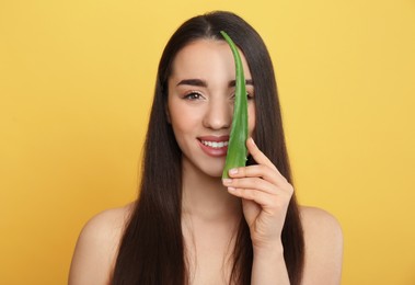 Young woman with aloe vera leaf on yellow background