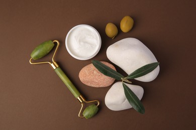 Photo of Flat lay composition with jar of cream, face roller and stones on brown background
