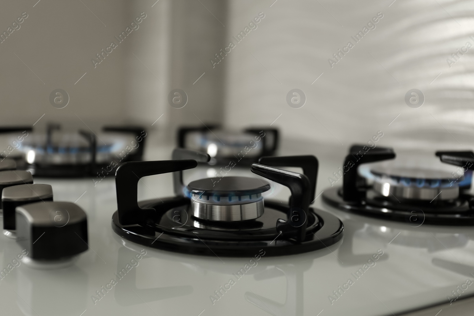 Photo of Gas burners with blue flame on modern stove, closeup