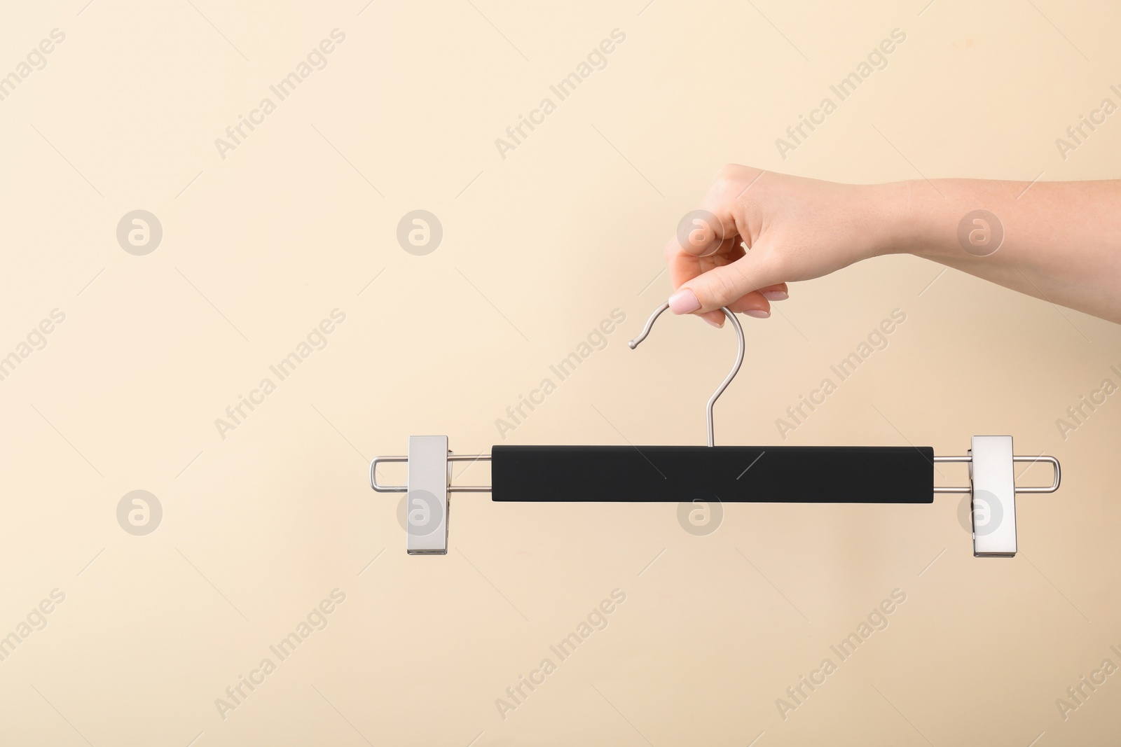 Photo of Woman holding hanger with clips on beige background, closeup. Space for text
