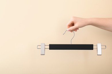 Woman holding hanger with clips on beige background, closeup. Space for text