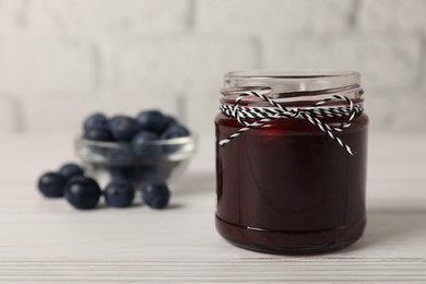 Photo of Jar of delicious blueberry jam on white wooden table, closeup. Space for text