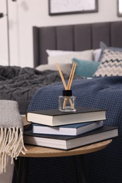 Aromatic reed air freshener, books and plaid on table, space for text