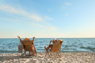 Young couple relaxing in deck chairs on beach near sea