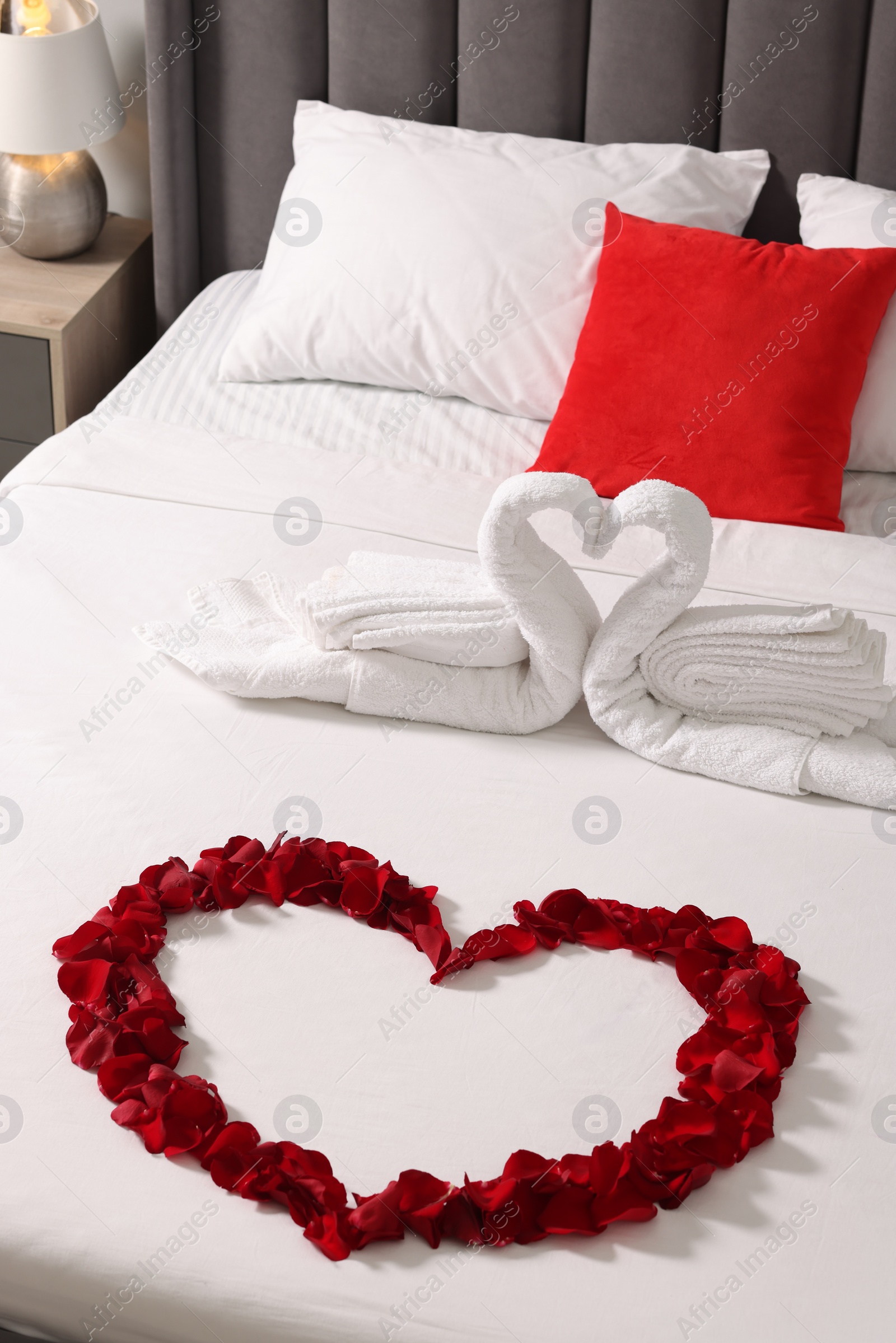 Photo of Honeymoon. Swans made with towels and heart of beautiful rose petals on bed in room