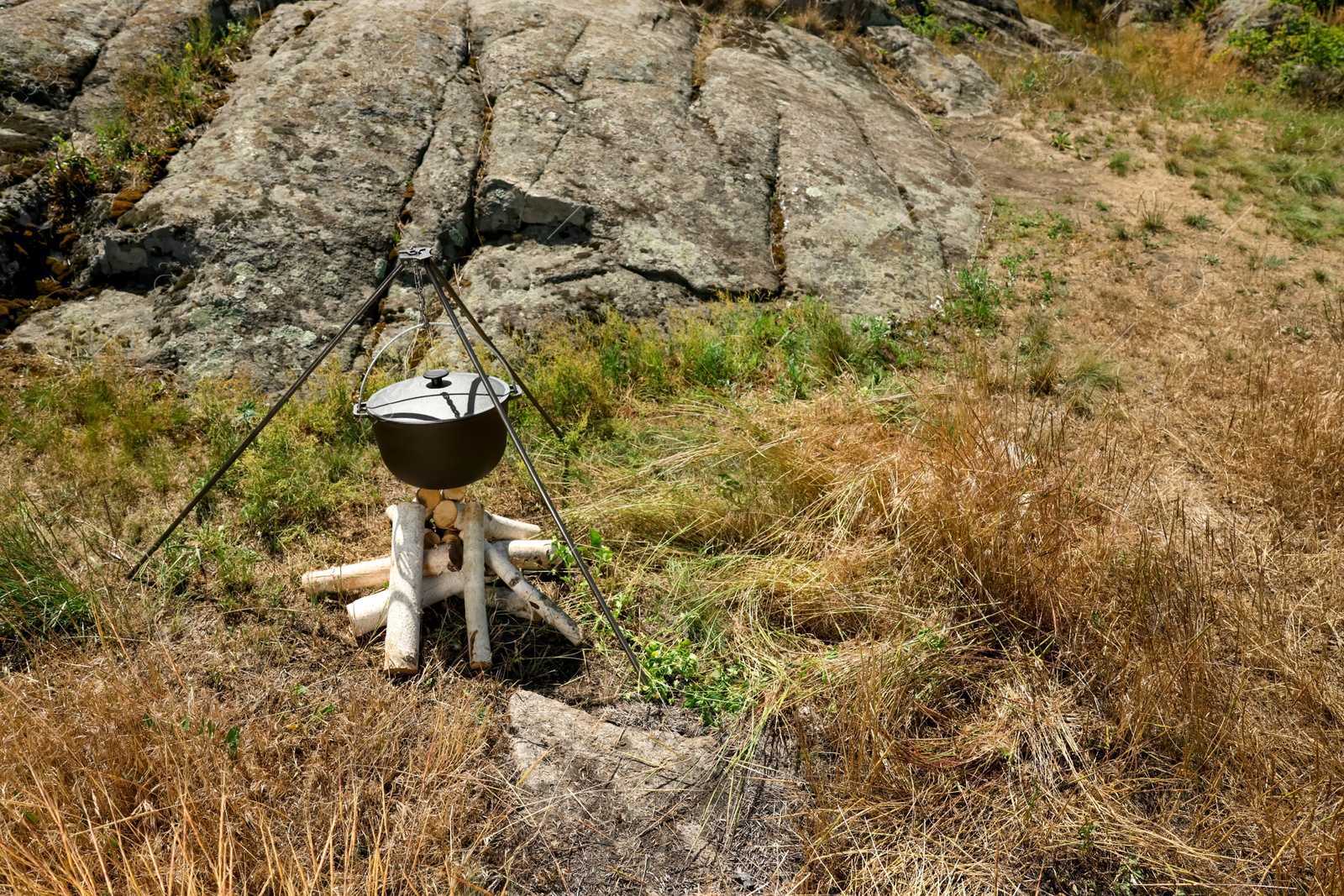 Photo of Cauldron above dry firewood arranged for bonfire outdoors. Camping season