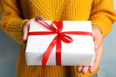 Young woman holding Christmas gift on blue background, closeup