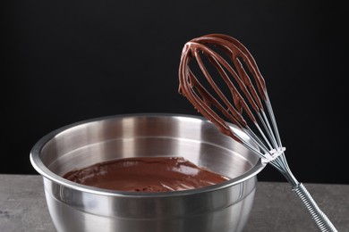 Photo of Bowl and whisk with chocolate cream on grey table against black background, closeup