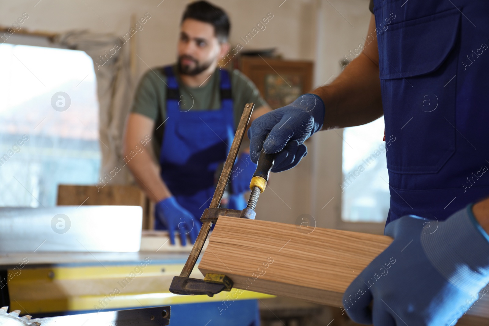 Photo of Professional carpenter with wooden board and clamp in workshop, closeup