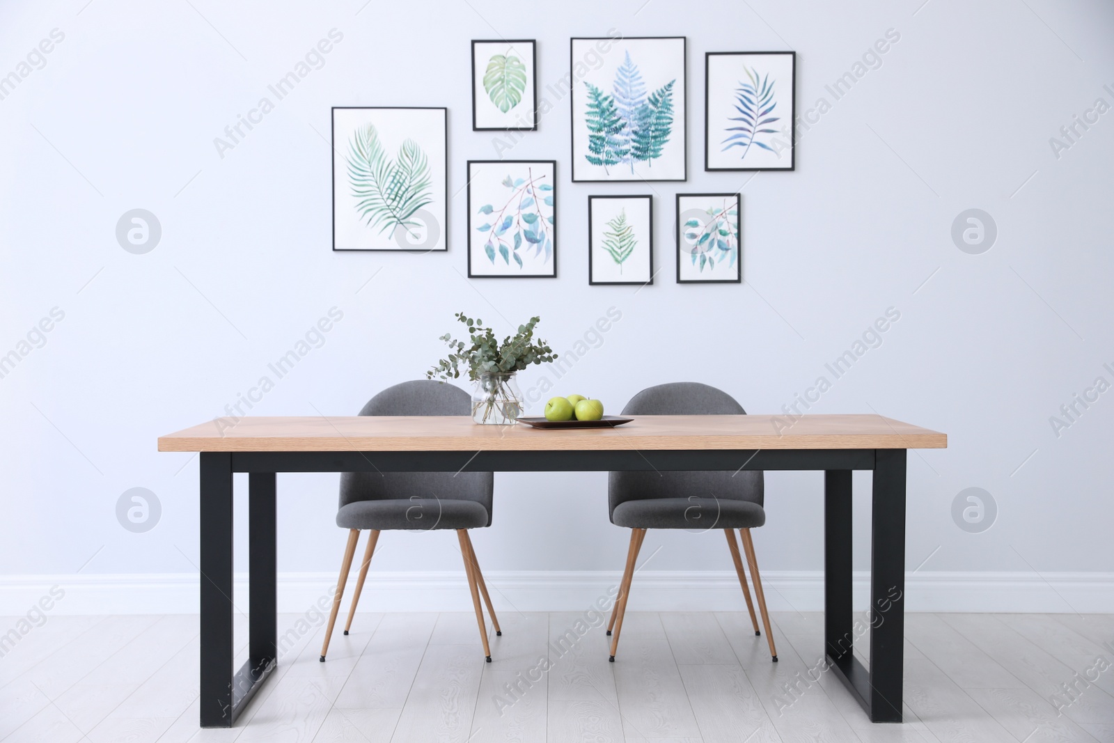 Photo of Stylish room interior with modern table, chairs and paintings of tropical leaves. Idea for design