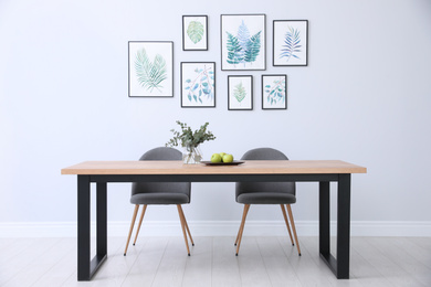 Stylish room interior with modern table, chairs and paintings of tropical leaves. Idea for design