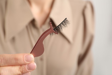 Photo of Woman holding tweezers with magnetic eyelashes, closeup