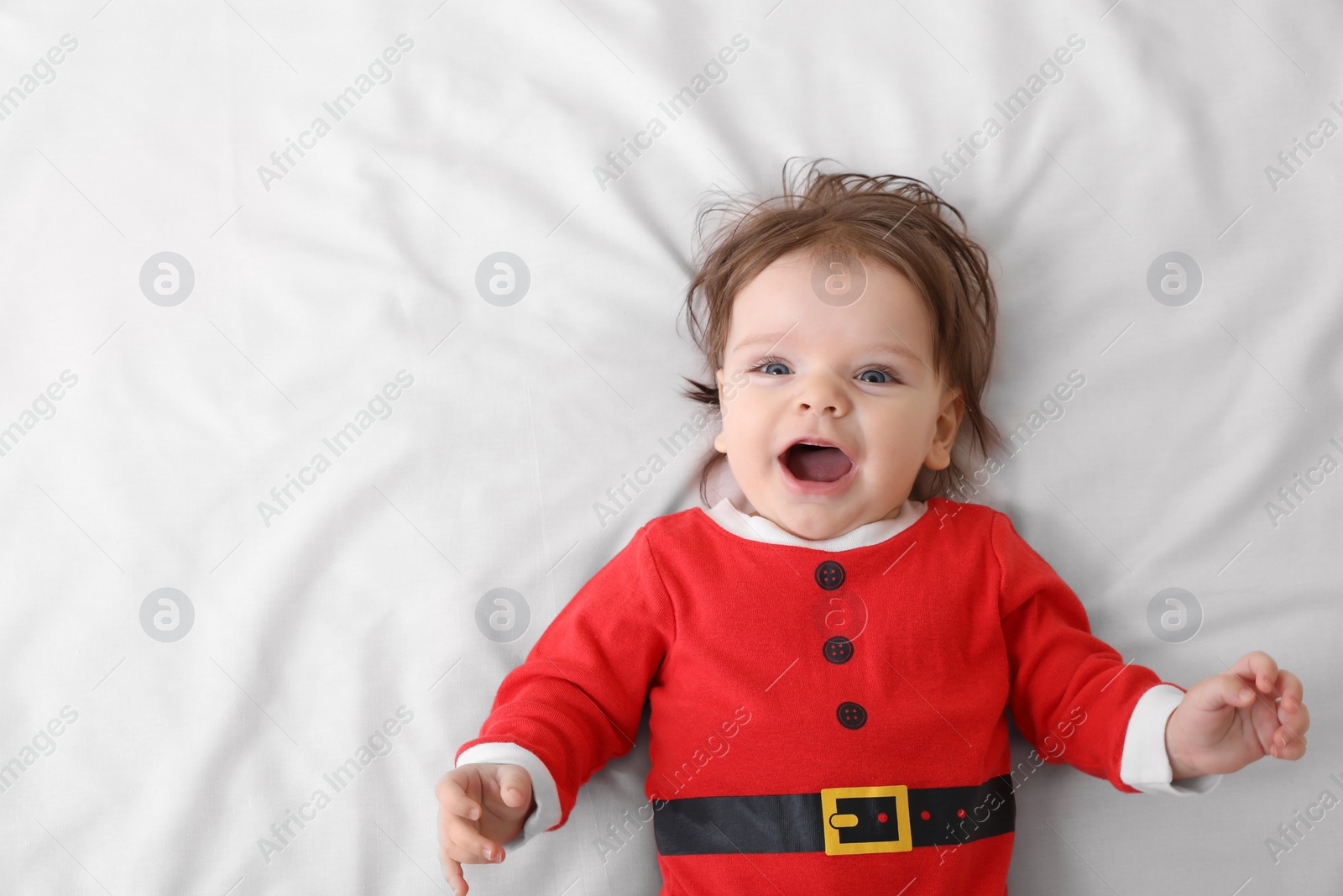 Photo of Cute baby wearing festive Christmas costume on white bedsheet, top view. Space for text