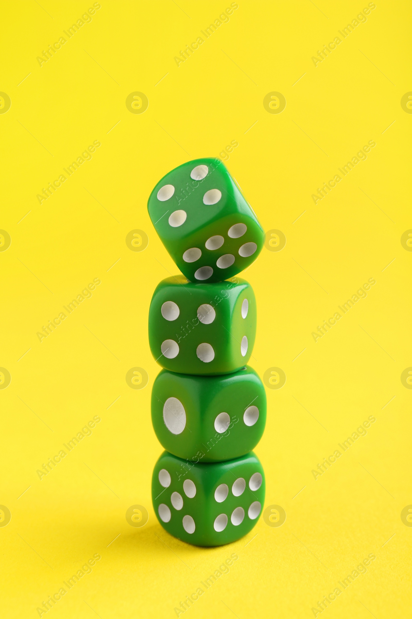 Photo of Many stacked green game dices on yellow background, closeup