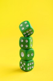 Photo of Many stacked green game dices on yellow background, closeup